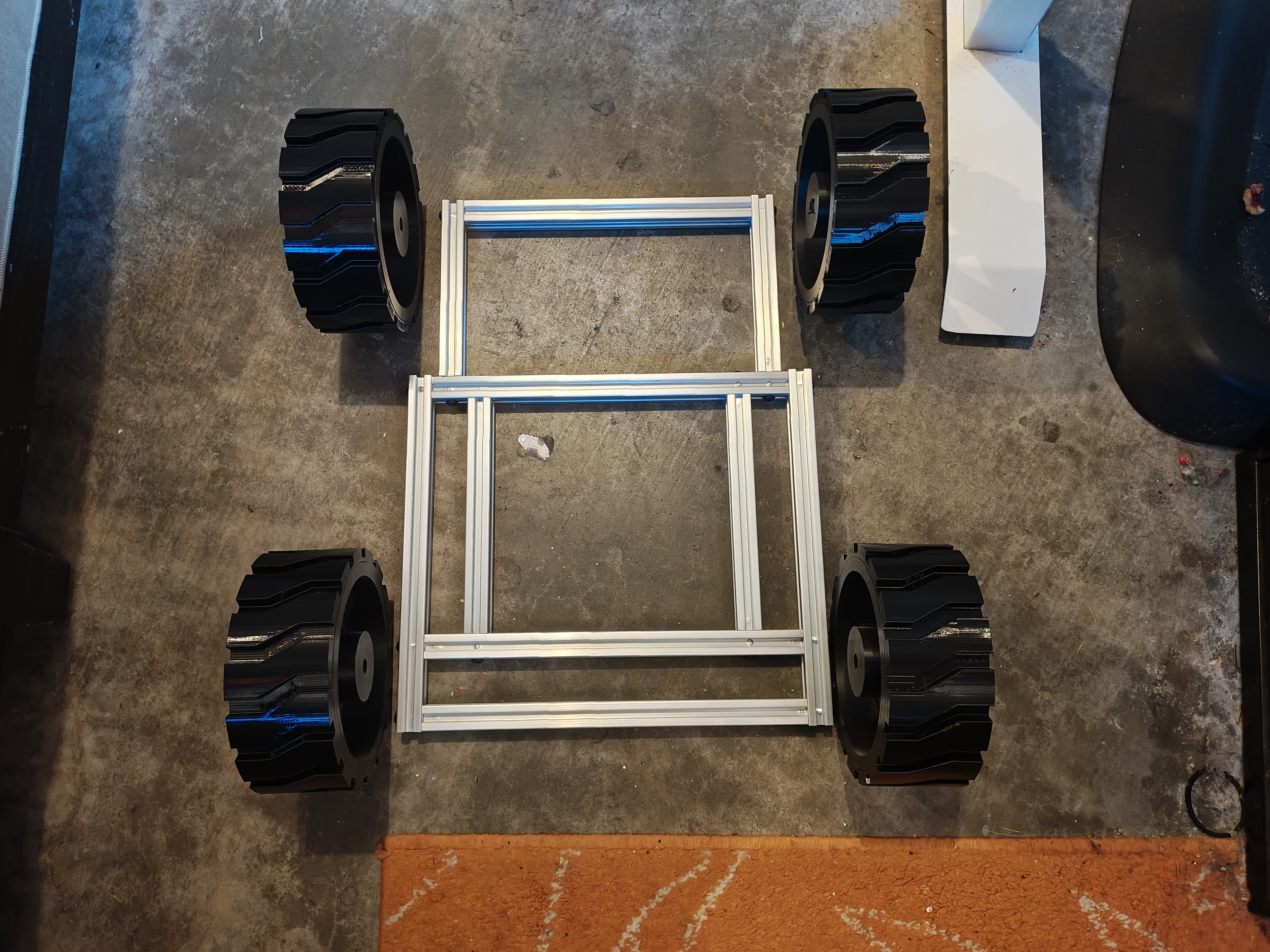 Rectangular aluminum frame on garage floor with four large black wheels placed at the corners