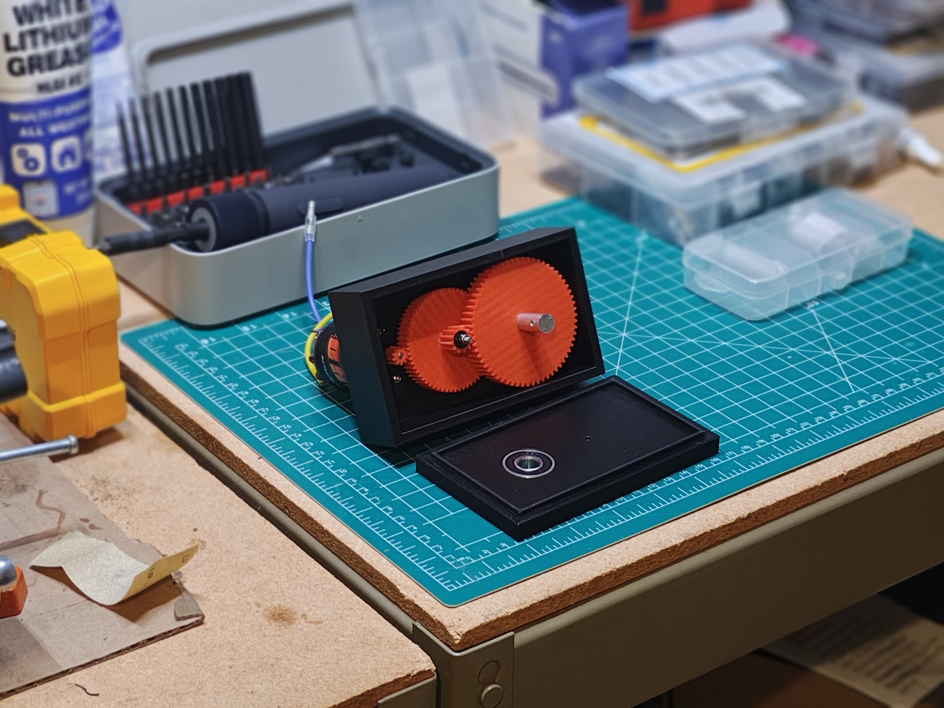 Black 3D-printed gearbox enclosure with lid open, showing two red spur gears and output shaft