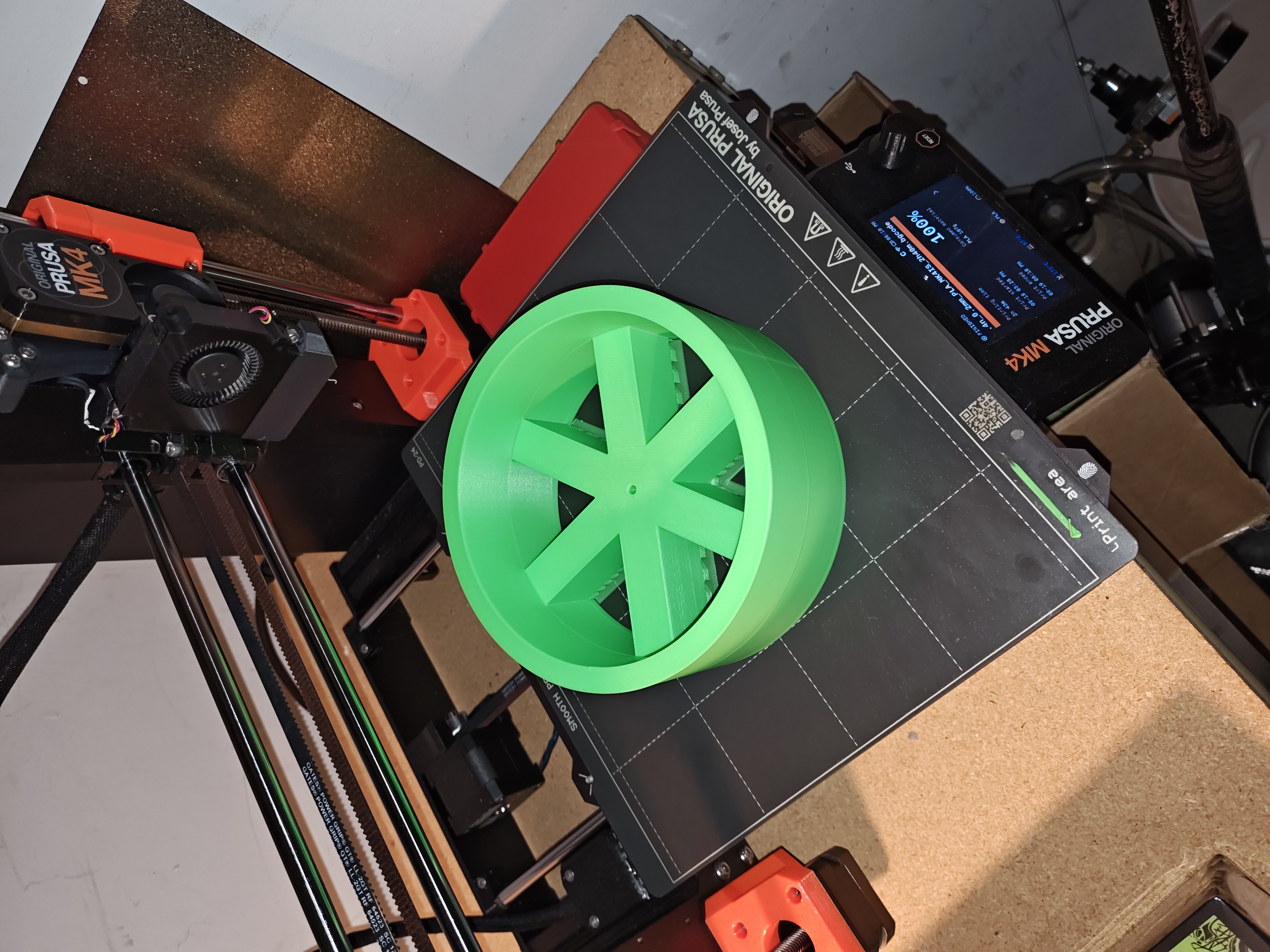 White PLA wheel hub sitting on 3D printer bed with honeycomb infill pattern visible