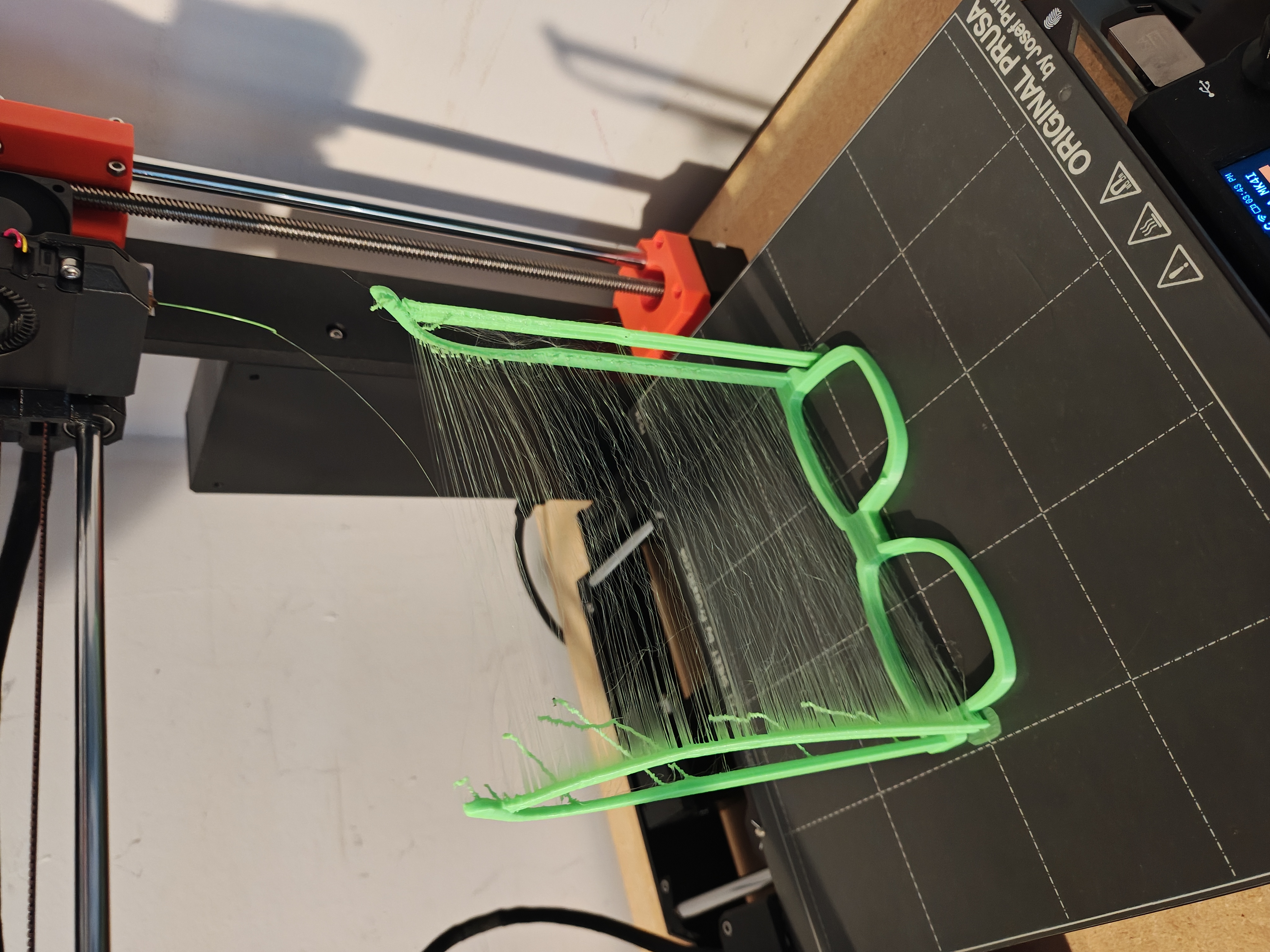 Failed glasses print on Prusa printer bed with heavy stringing