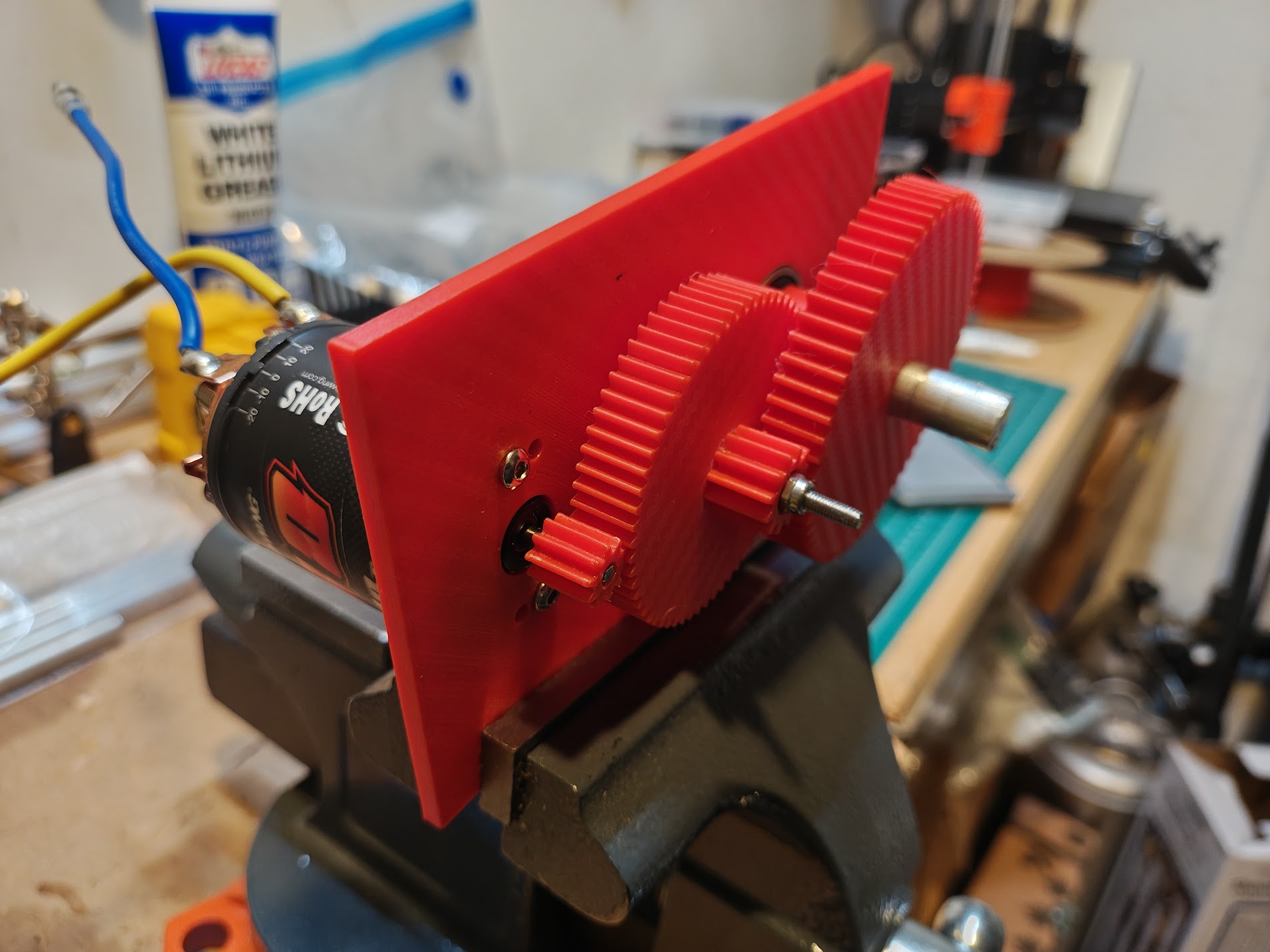 Red 3D-printed 2-stage gearbox with motor attached, held in a vise on workbench