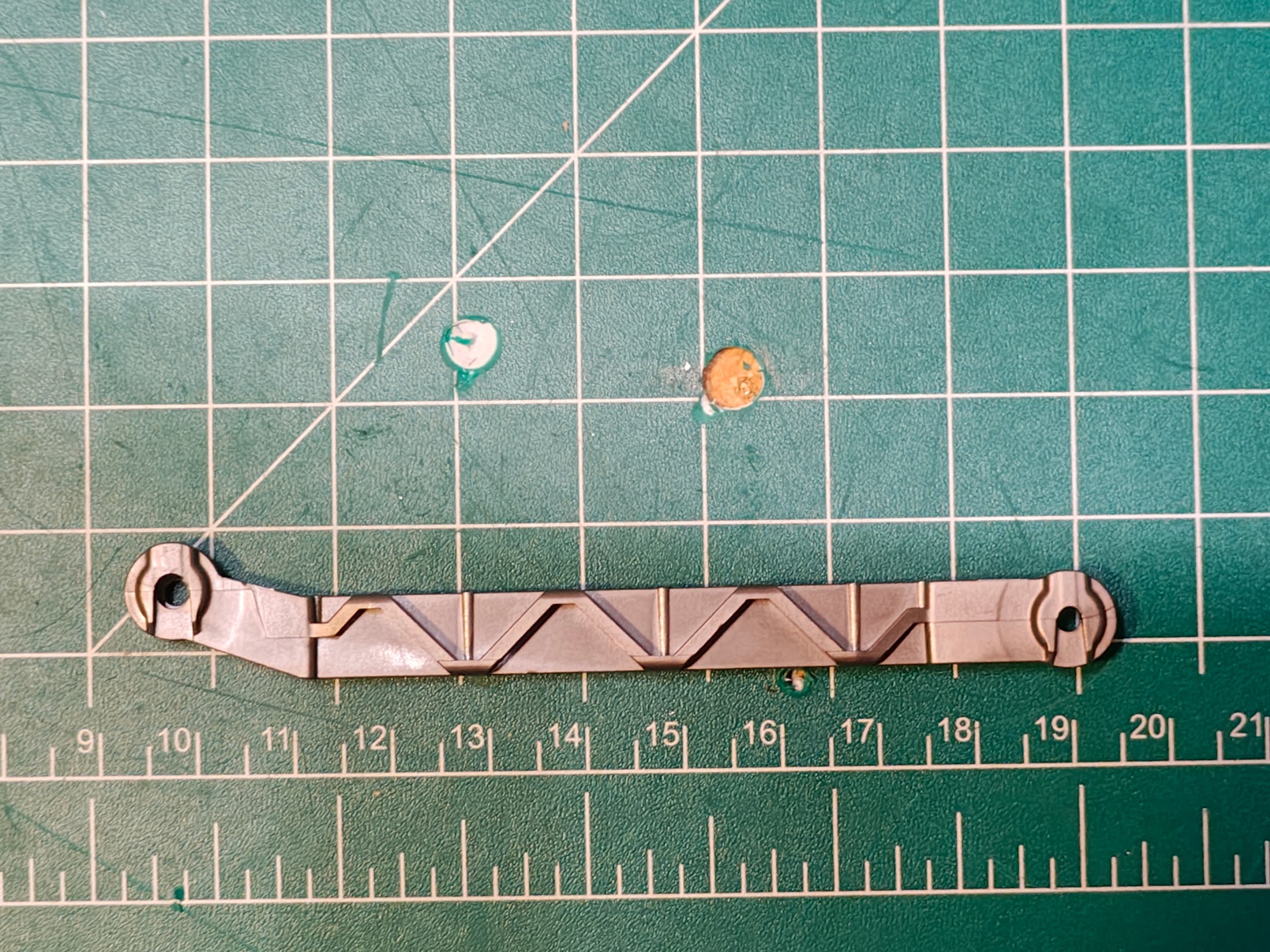 Broken garbage can grabber linkage on cutting mat, front view