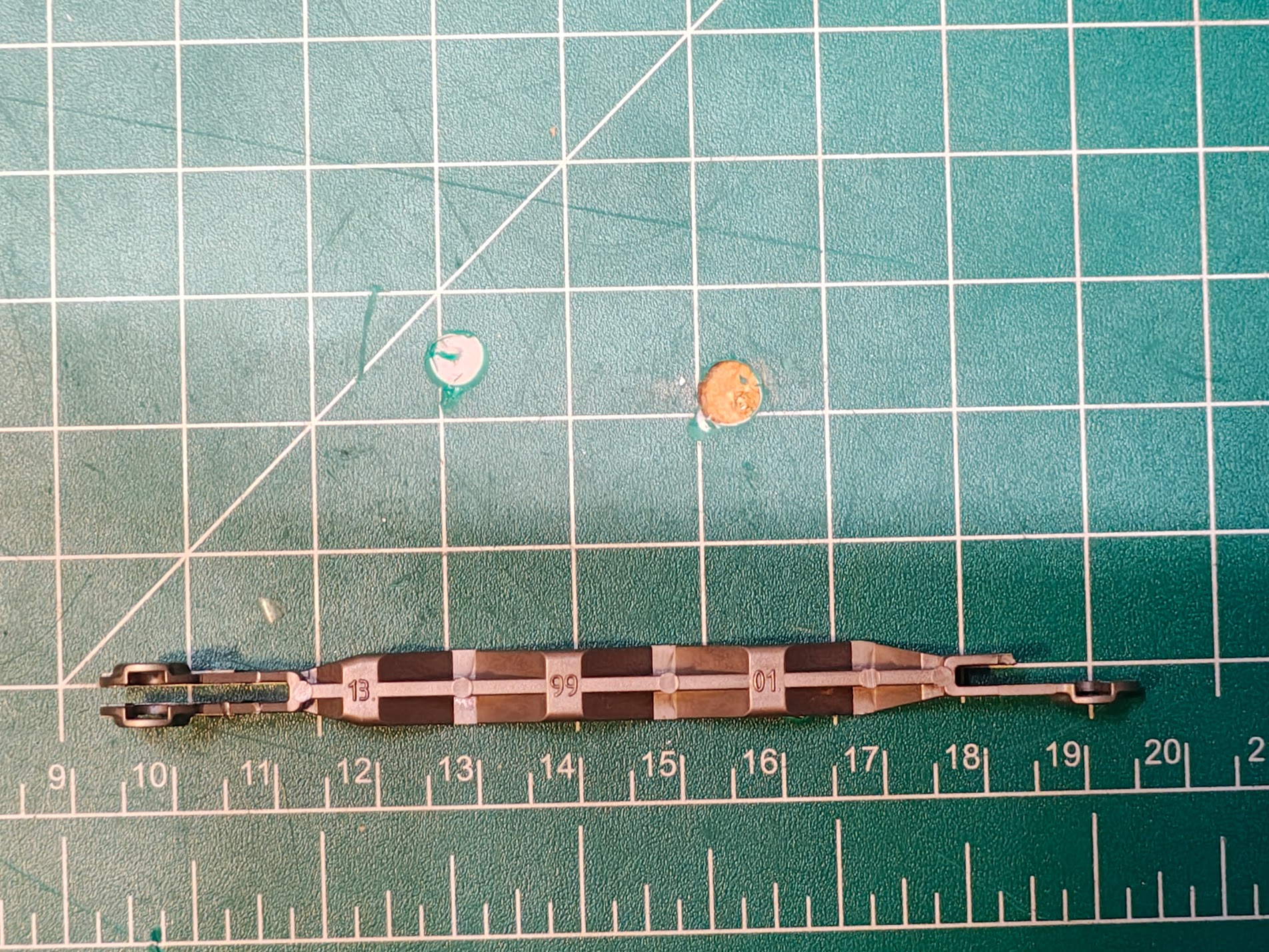 Broken garbage can grabber linkage on cutting mat, top view